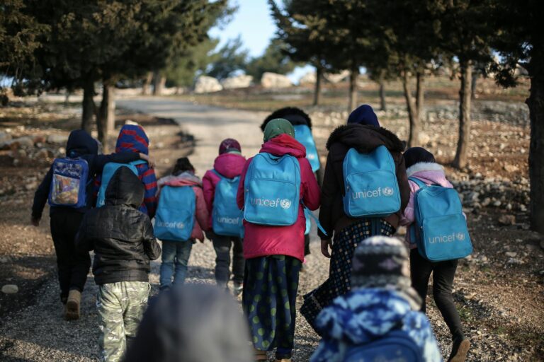 A group of children with UNICEF backpacks walking on a dirt road in rural Syria.